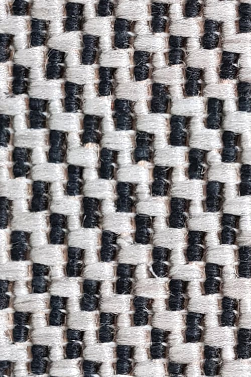 Close-up ofa rough carpet with black but mostly white fibers arranged in a zigzag pattern
