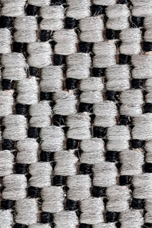 Close-up of a rough carpet with chunky black and mostly white fibers arranged in a zigzag pattern