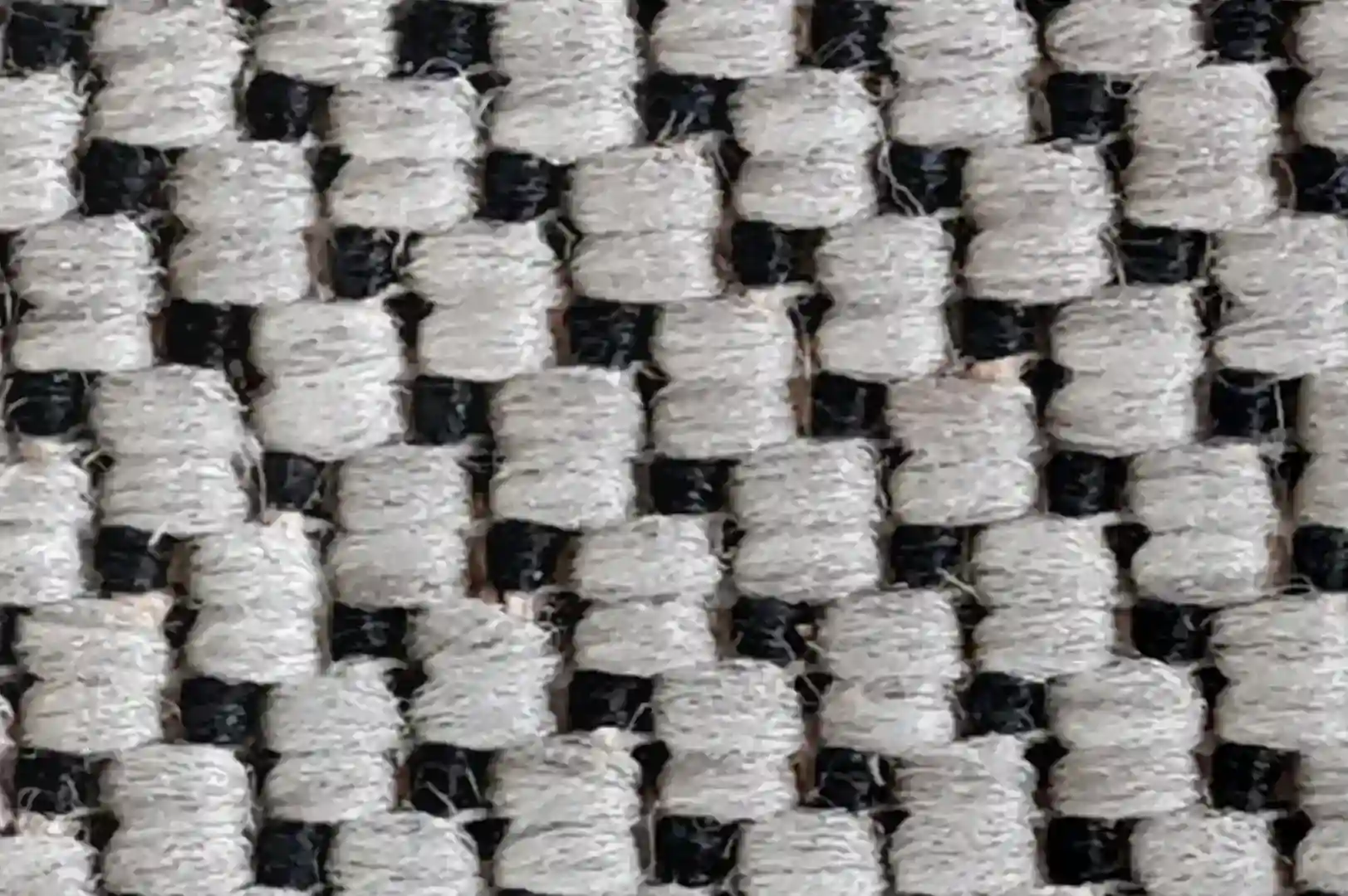 Close-up of a rough carpet with chunky black and mostly white fibers arranged in a zigzag pattern