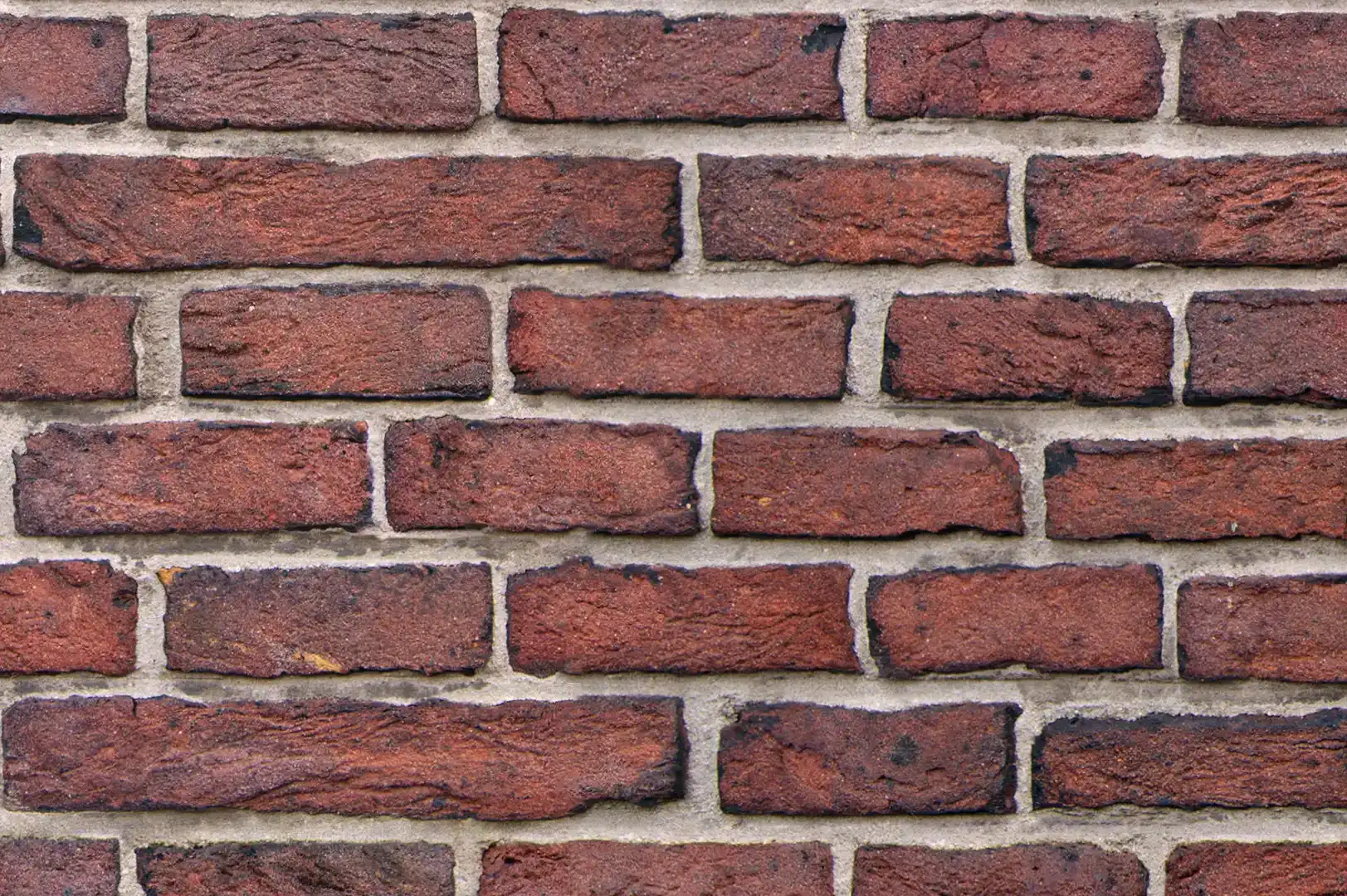 Close-up of a dark red brick wall with coarse surface