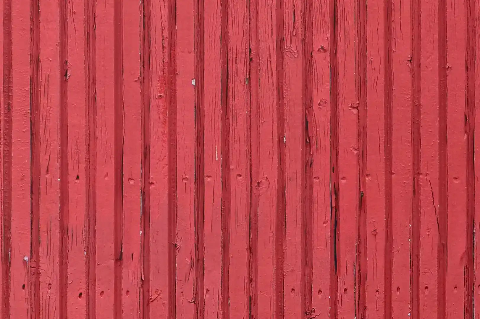 Close-up of an exterior vertical wood paneling with red flaking paint