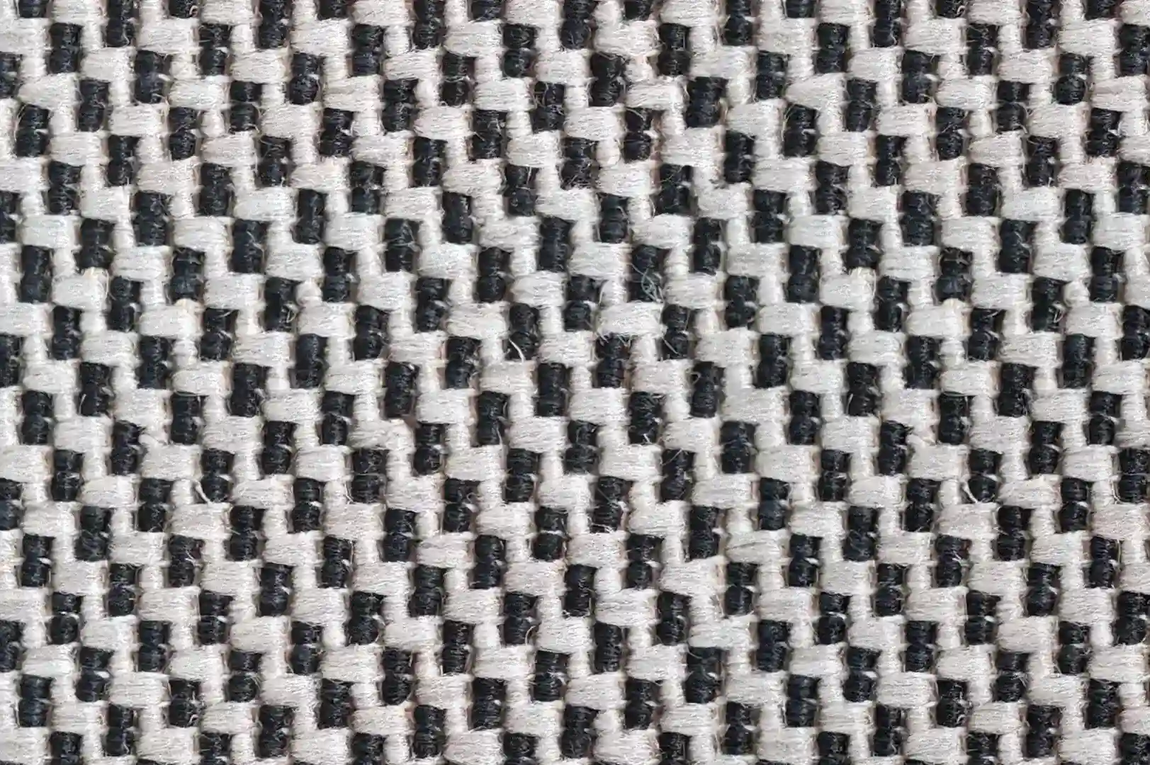 Close-up ofa rough carpet with black but mostly white fibers arranged in a zigzag pattern