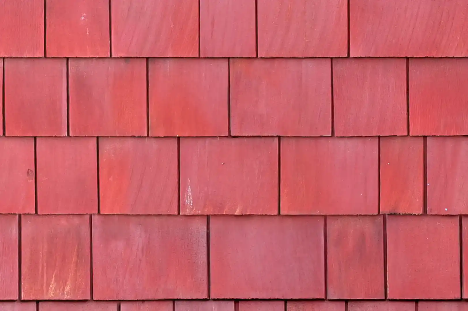 Close-up of a vertical wall covered with red painted rough wood shingles